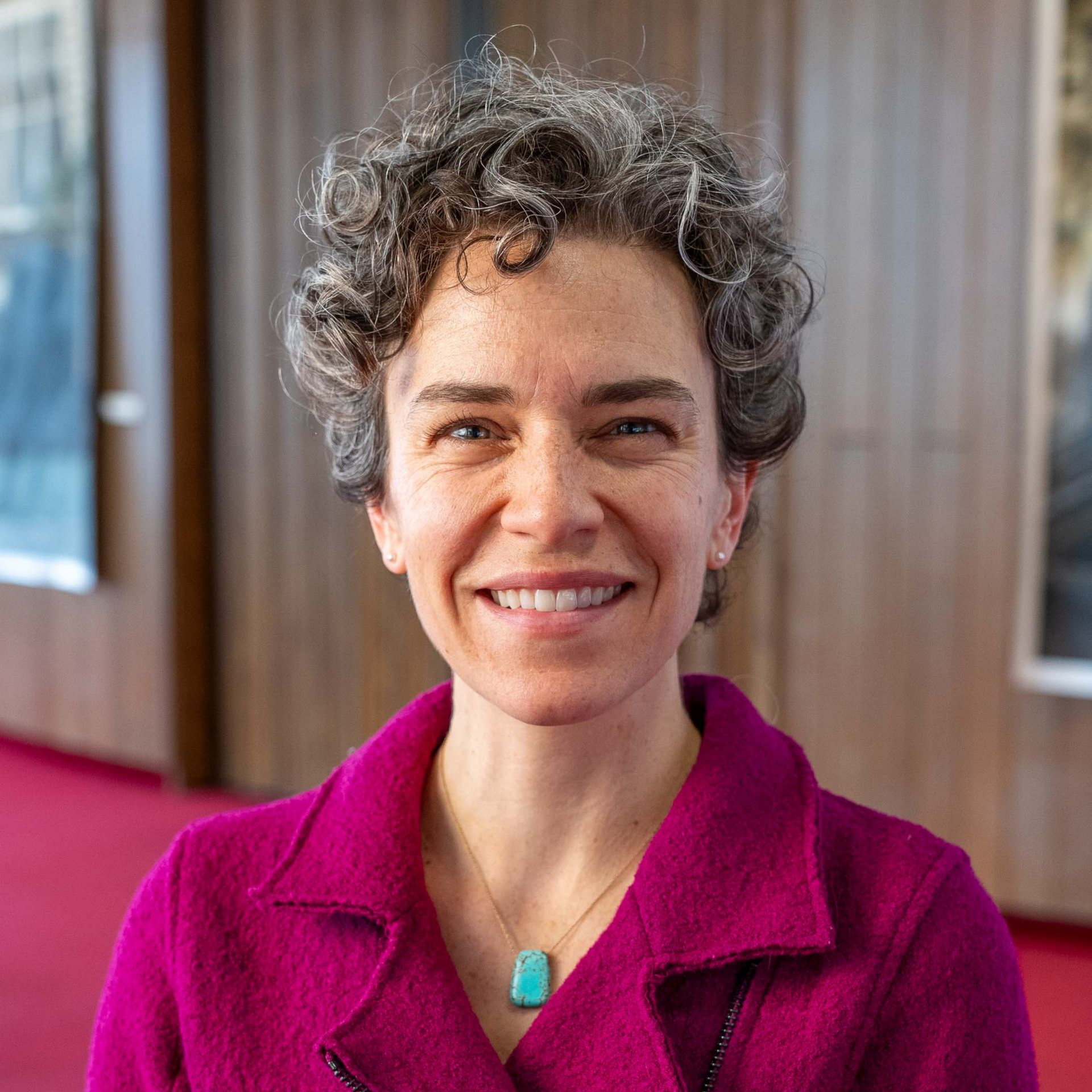 Smiling person in a magenta sweater indoors against a softly blurred background