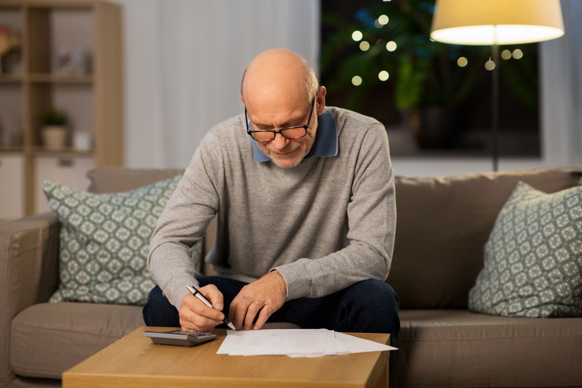 A man is sitting on a couch using a calculator and writing on a piece of paper.