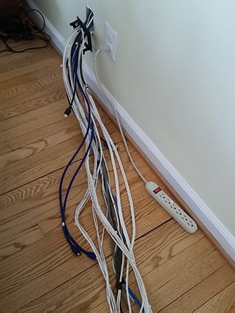 Bundle of white and blue cables running along a wall to a power strip on a hardwood floor