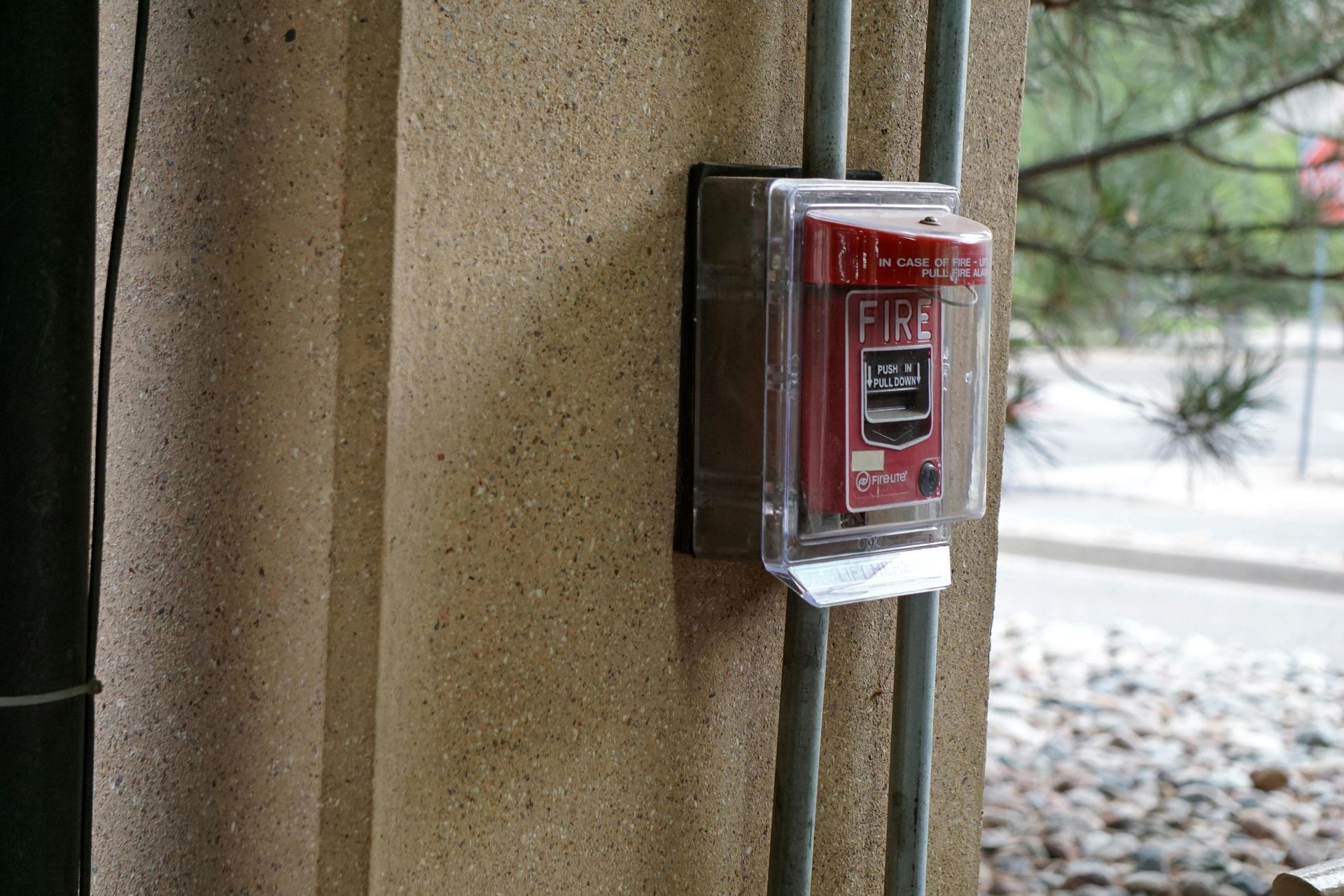 Red fire alarm box mounted on an outdoor wall beside a covered walkway