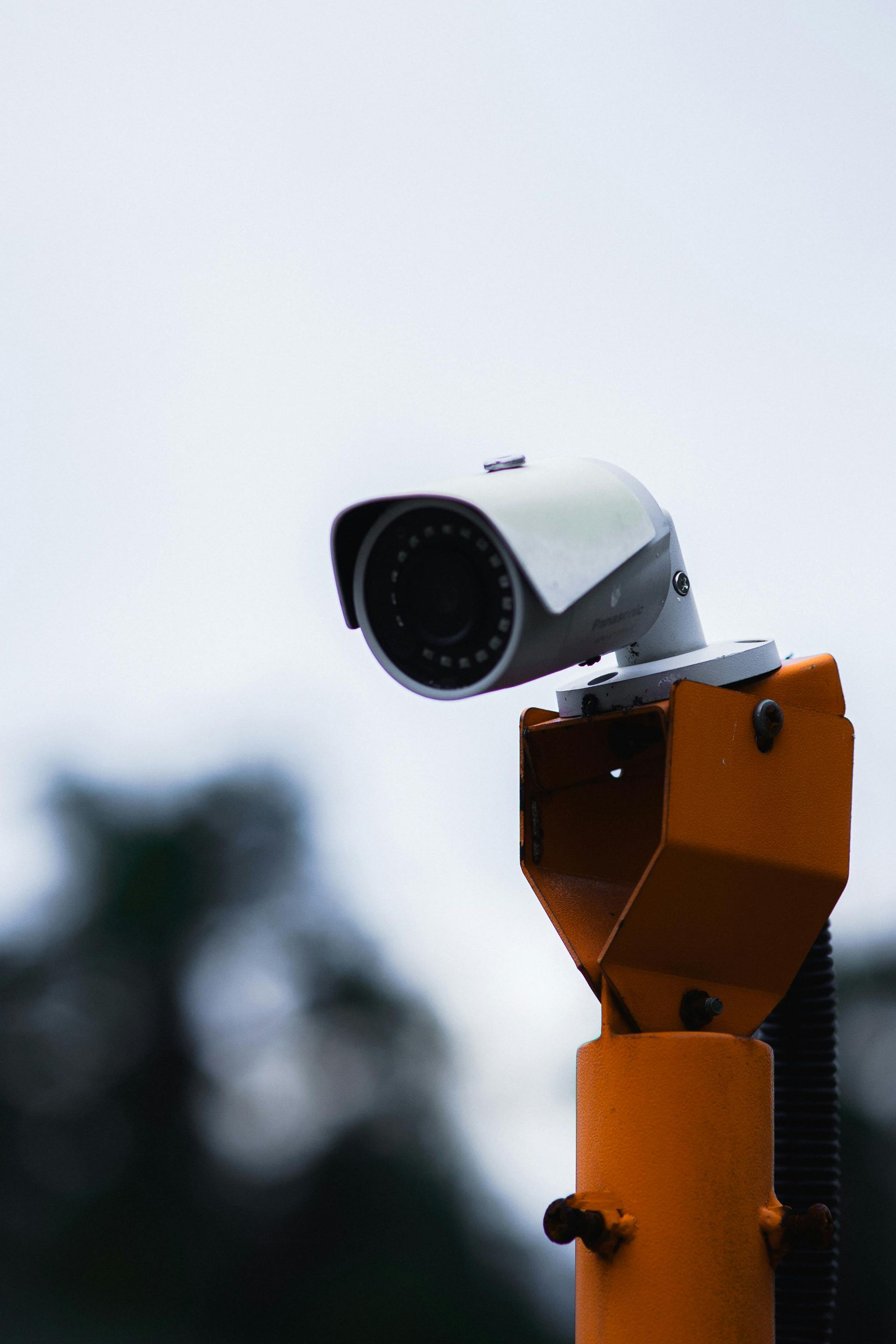 Orange security camera mounted on a pole against a cloudy sky