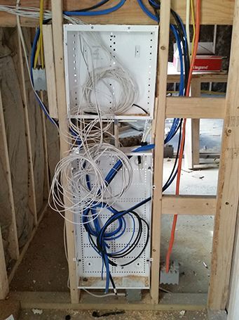 Open network wiring panel with tangled white and blue cables in unfinished wall framing