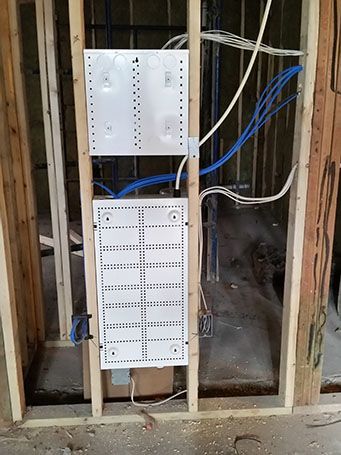 Open wall framing with two white electrical panels and blue wiring in a renovation area