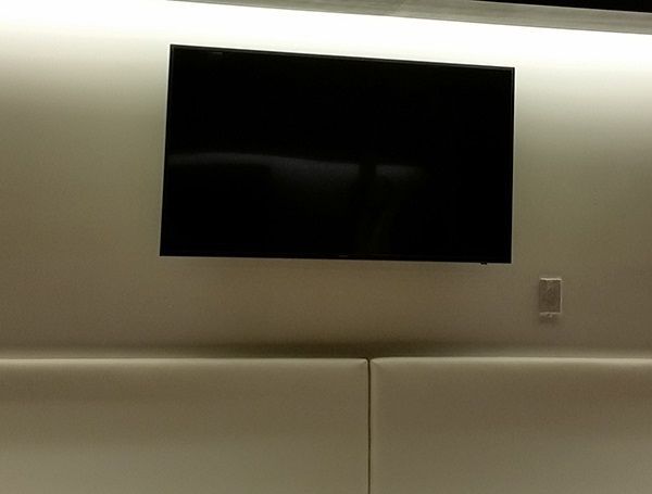 Wall-mounted black TV above a beige upholstered headboard in a softly lit room