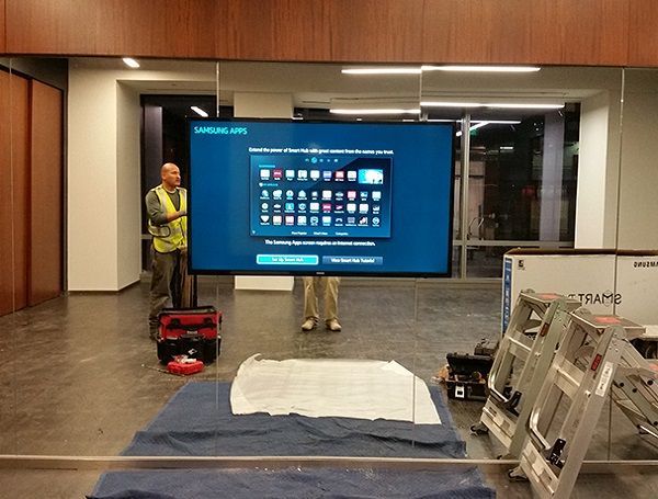 Airport lobby with a large digital screen, workers, and equipment on the floor covered by a tarp.