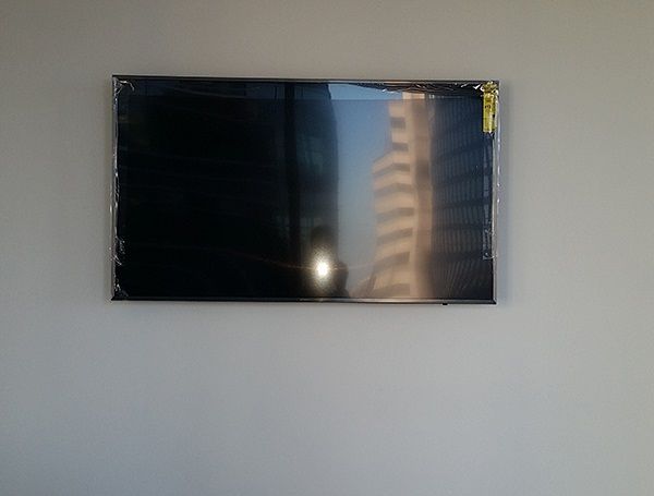 Black wall-mounted TV on a plain white wall, reflecting a nearby building.
