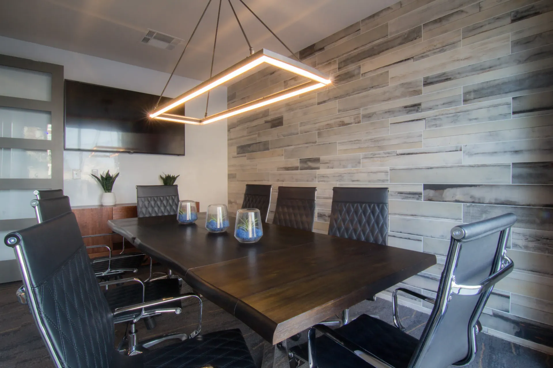 Modern conference room with a long dark wood table and black leather chairs under a rectangular pendant light.