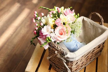 A bouquet of soft pink and white flowers in a rustic wicker basket set on a wooden surface.