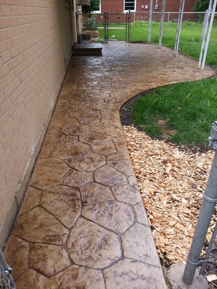 A concrete walkway leading to a backyard with a brick building in the background.