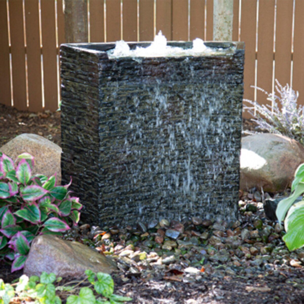 A water fountain in a garden with a wooden fence in the background