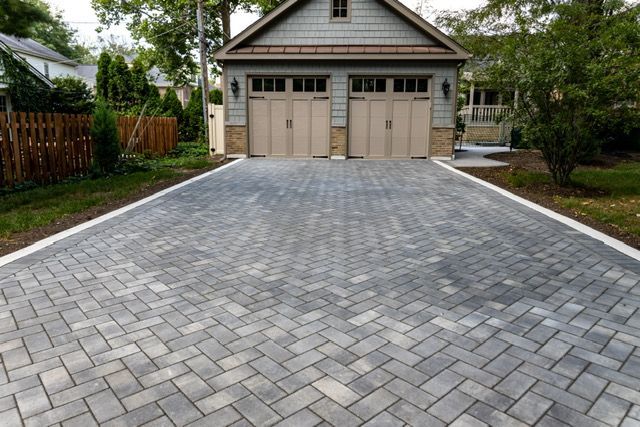 A brick driveway leading to a garage with two garage doors.