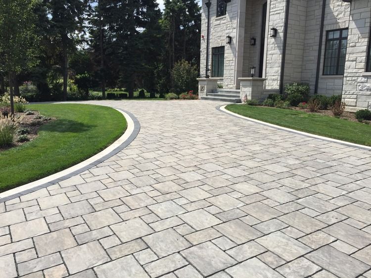 A brick driveway leading to a large house with a lush green lawn.