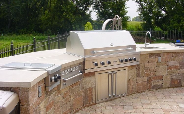 An outdoor kitchen with a stainless steel grill and sink