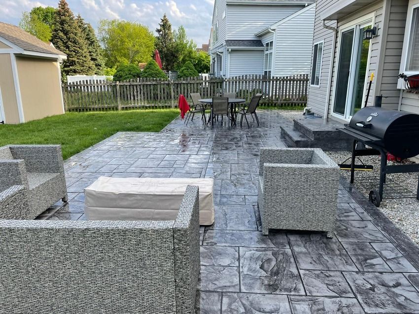 A patio with chairs , a table and a grill in the backyard of a house.