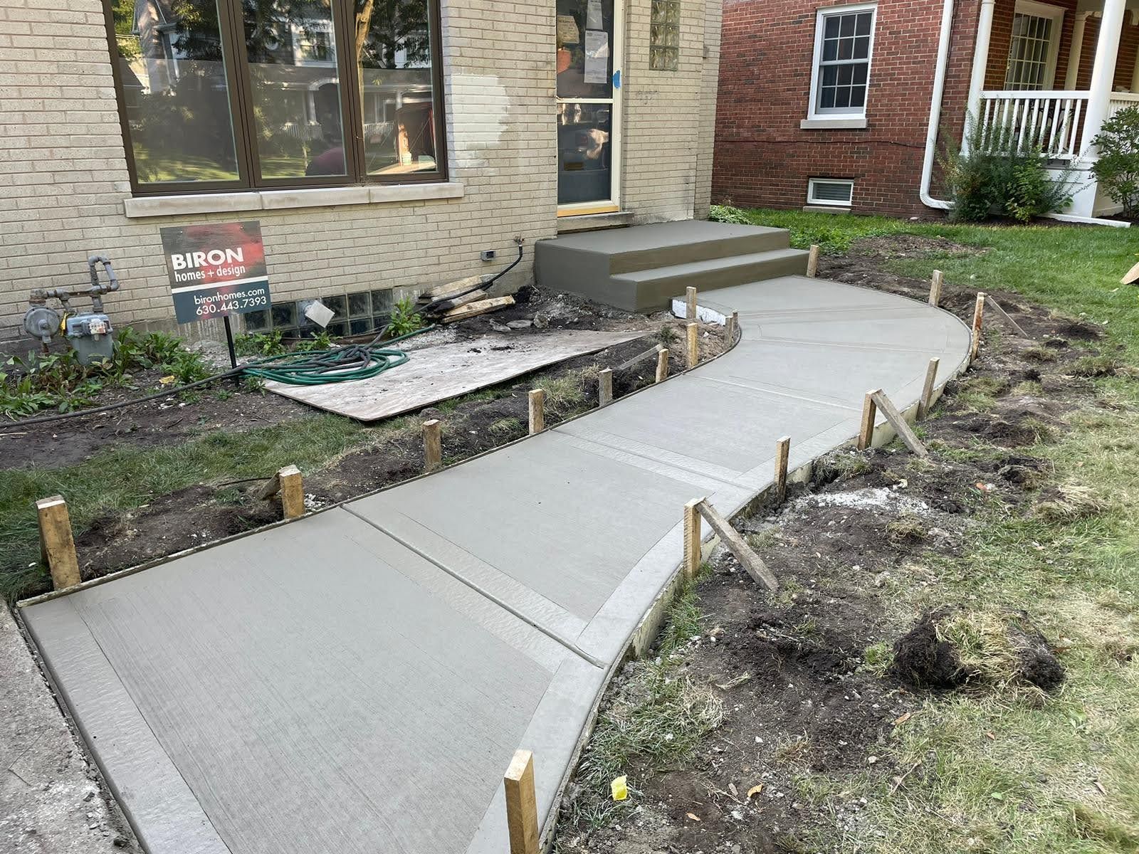 A concrete walkway is being built in front of a brick house.