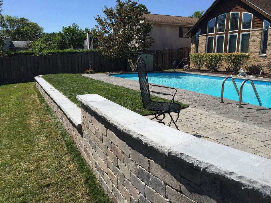 A brick wall surrounds a swimming pool in a backyard