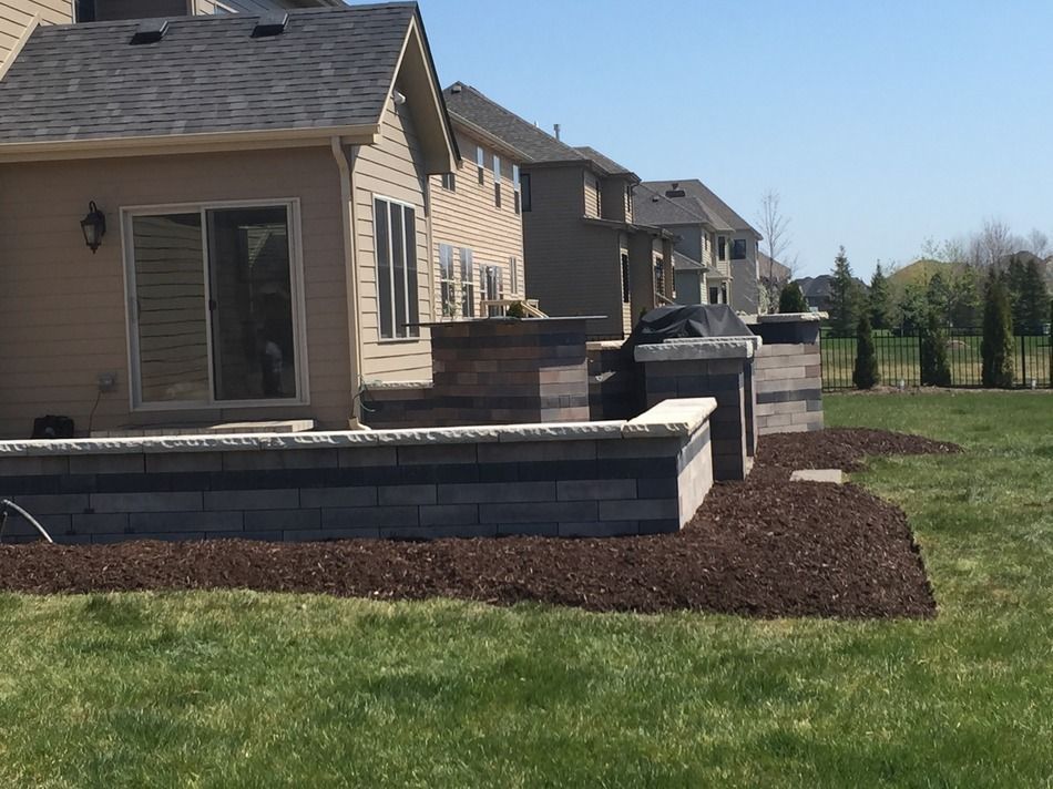 A backyard with a brick wall and a grill in front of a house.