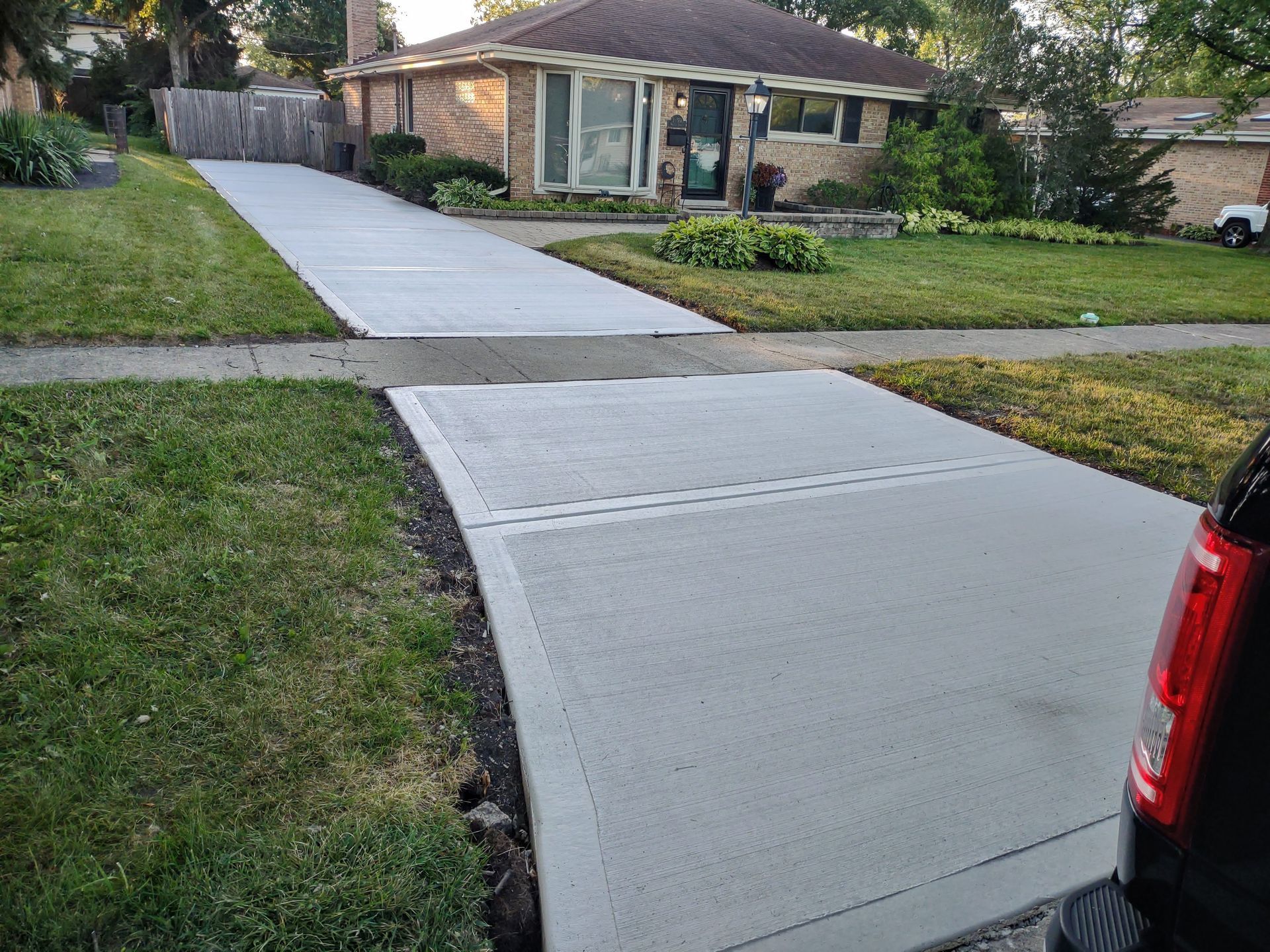 A concrete driveway leading to a house with a truck parked on the side of it.