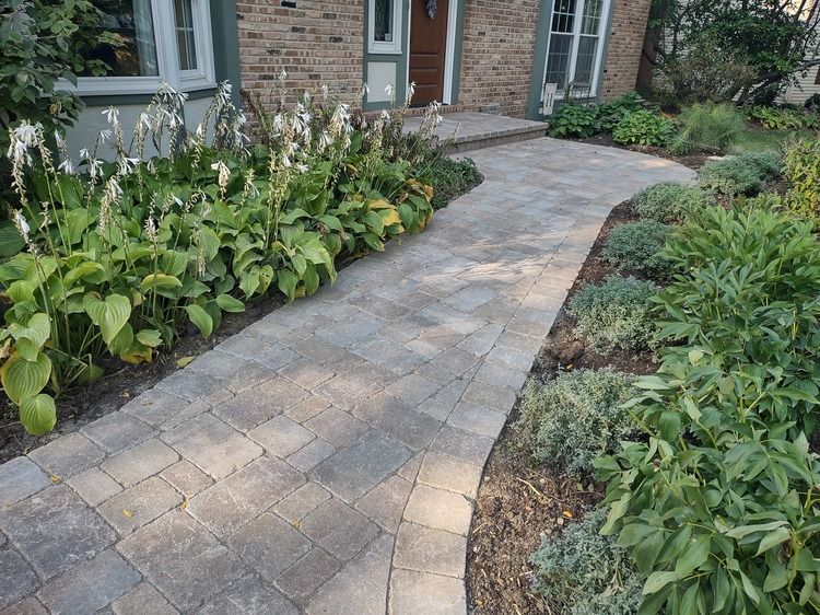 A brick walkway leading to a brick house surrounded by plants.