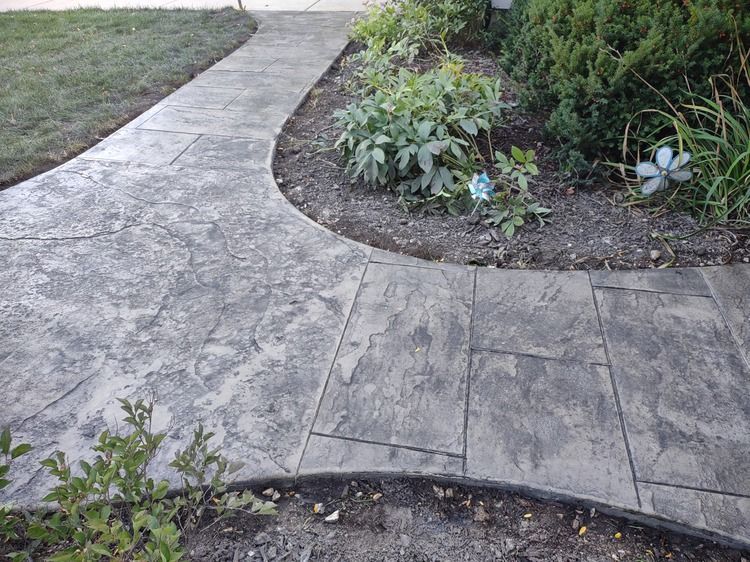 A concrete walkway leading to a garden with a flower in the middle.