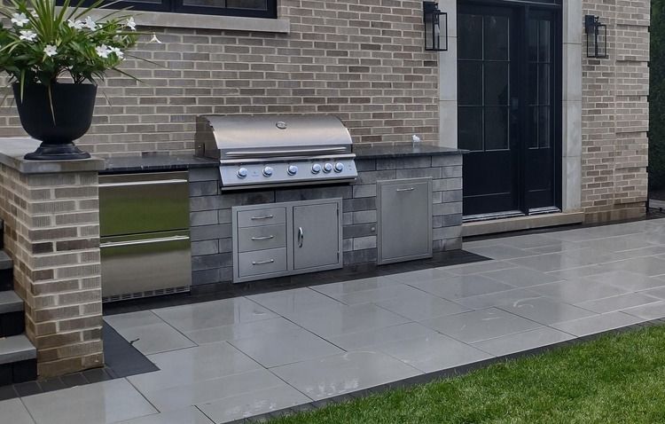 There is a grill in the backyard of a brick house.