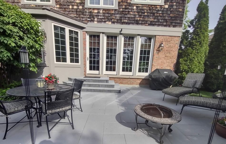 A patio with a table and chairs and a fire pit in front of a house.