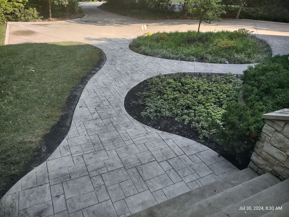 A concrete walkway leading to a driveway and a garden.