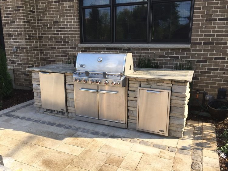 A stainless steel grill is sitting on a patio in front of a brick building.