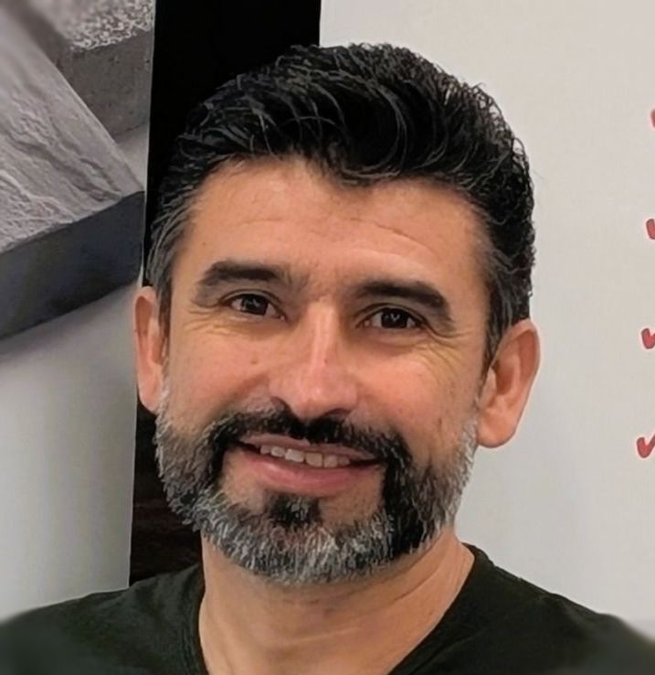 A man with a beard is wearing a white shirt and smiling.