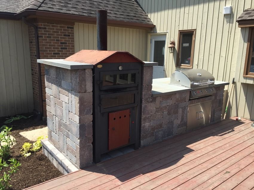 A pizza oven is sitting on a wooden deck in front of a house.