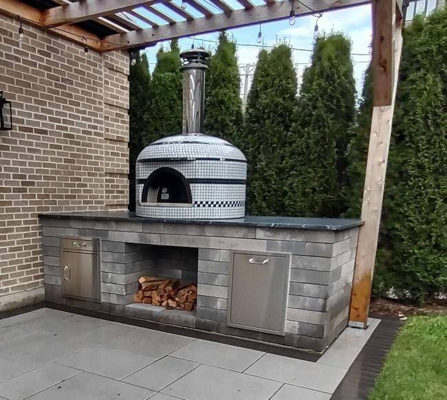 A pizza oven is sitting under a pergola on a patio.