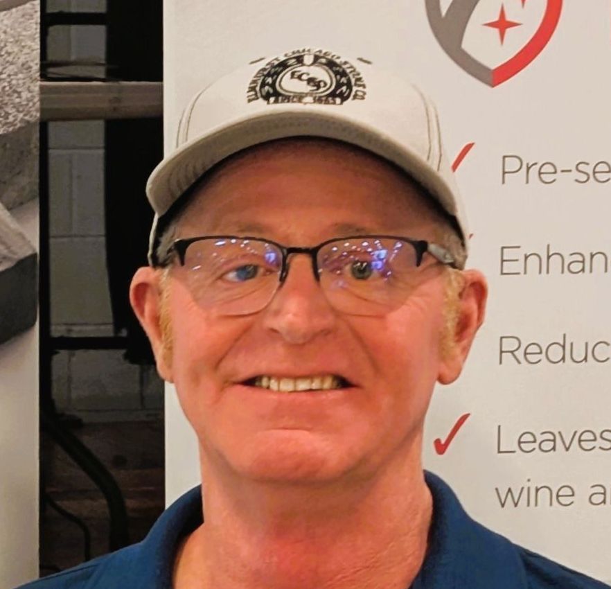 A man wearing glasses and a hat is smiling for the camera