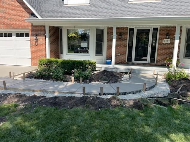 A brick house with a concrete walkway being built in front of it.