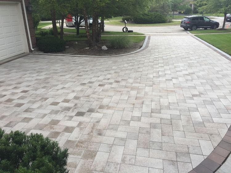 A brick driveway leading to a garage with a car parked in the driveway.