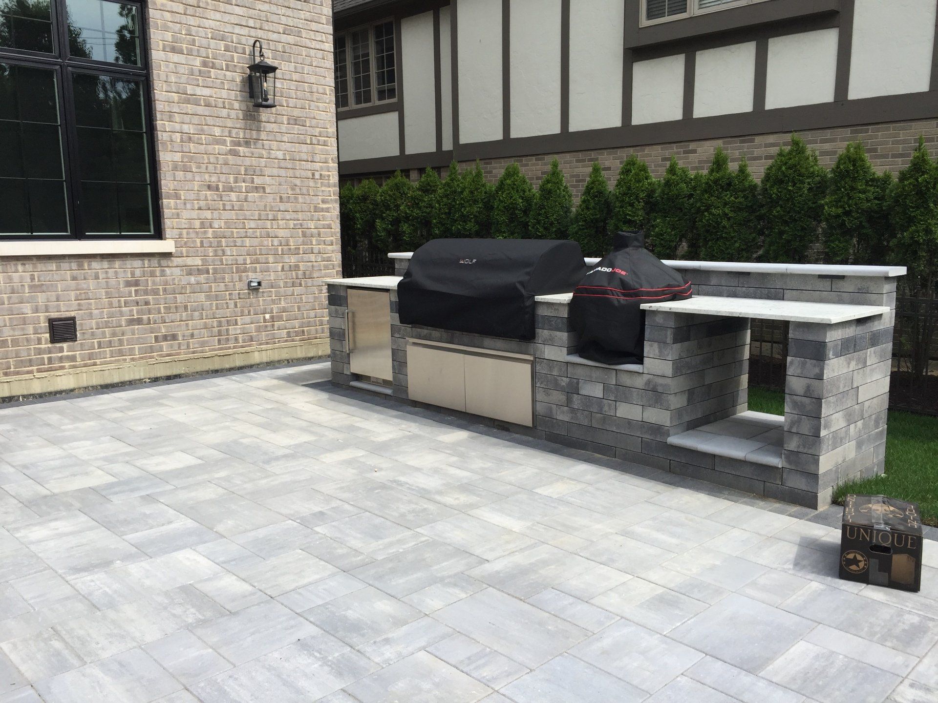 A large outdoor grill is sitting on a patio in front of a brick building.
