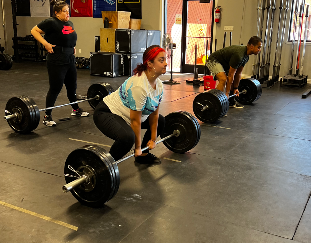 A group of people are squatting down with barbells in a gym.