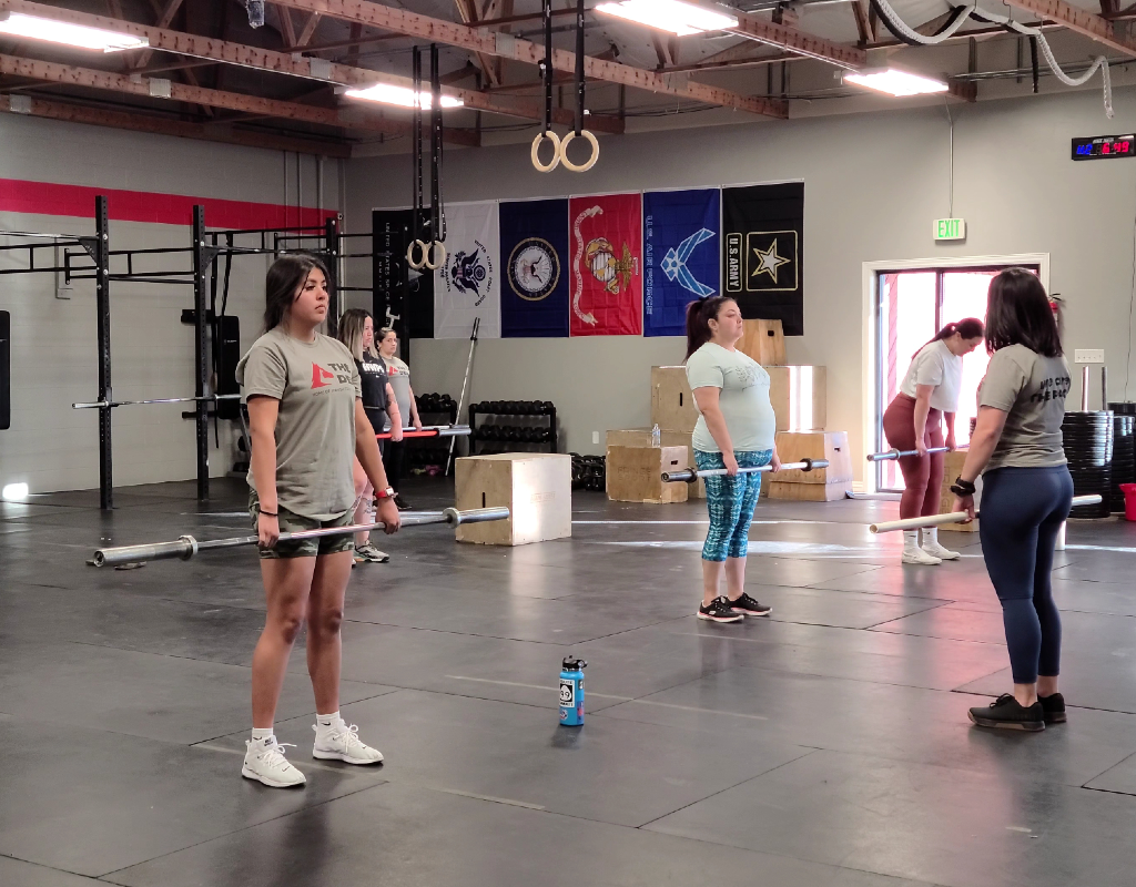 A group of women are standing in a gym holding barbells.