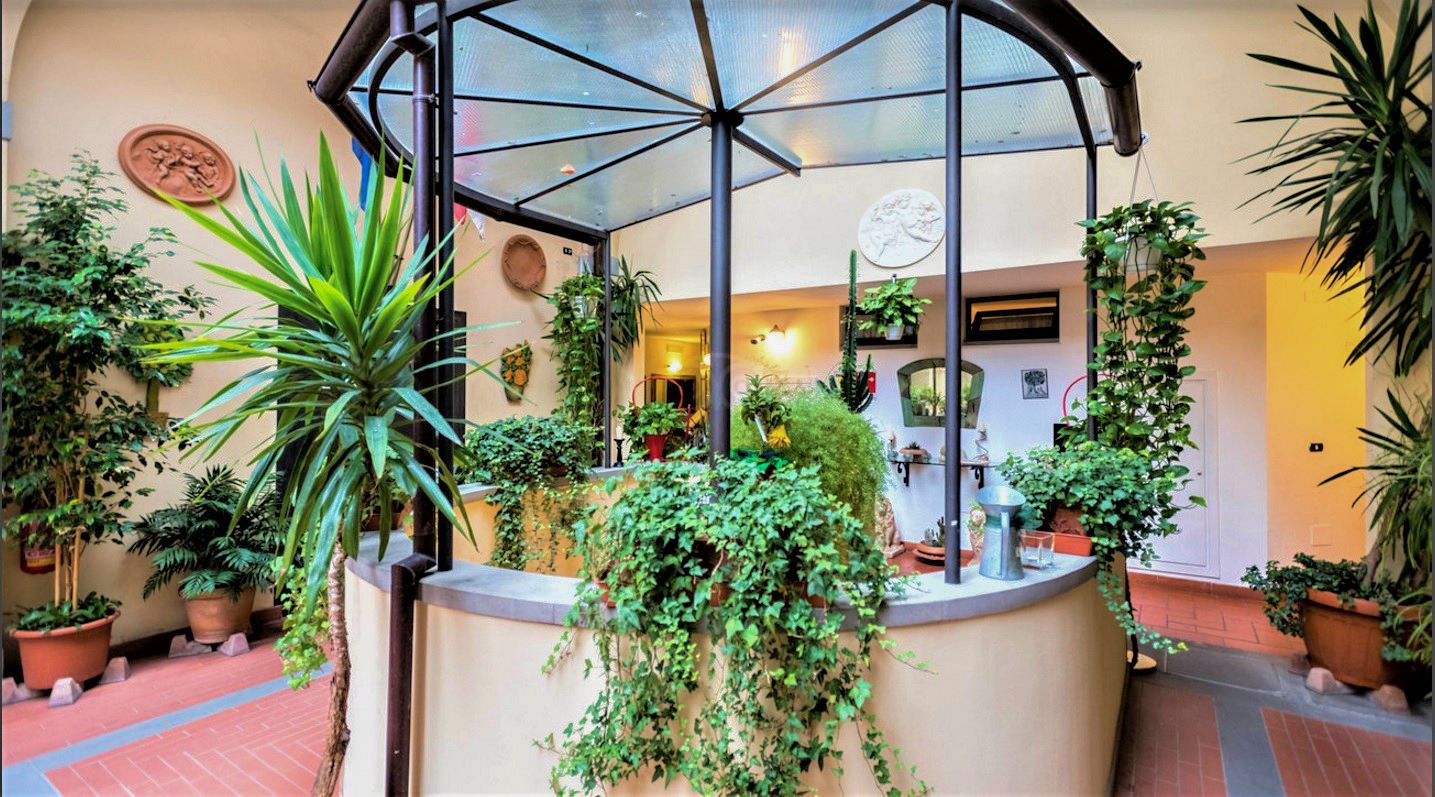 Indoor courtyard with a round fountain surrounded by lush potted plants and a glass canopy overhead