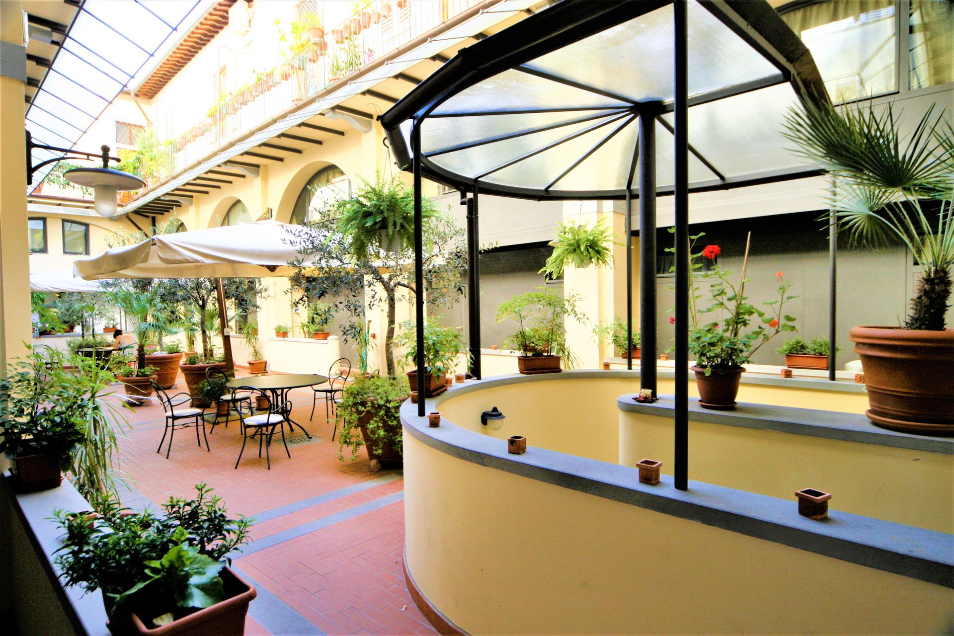 Courtyard cafe with tables and umbrellas beside a round yellow bar under a glass canopy