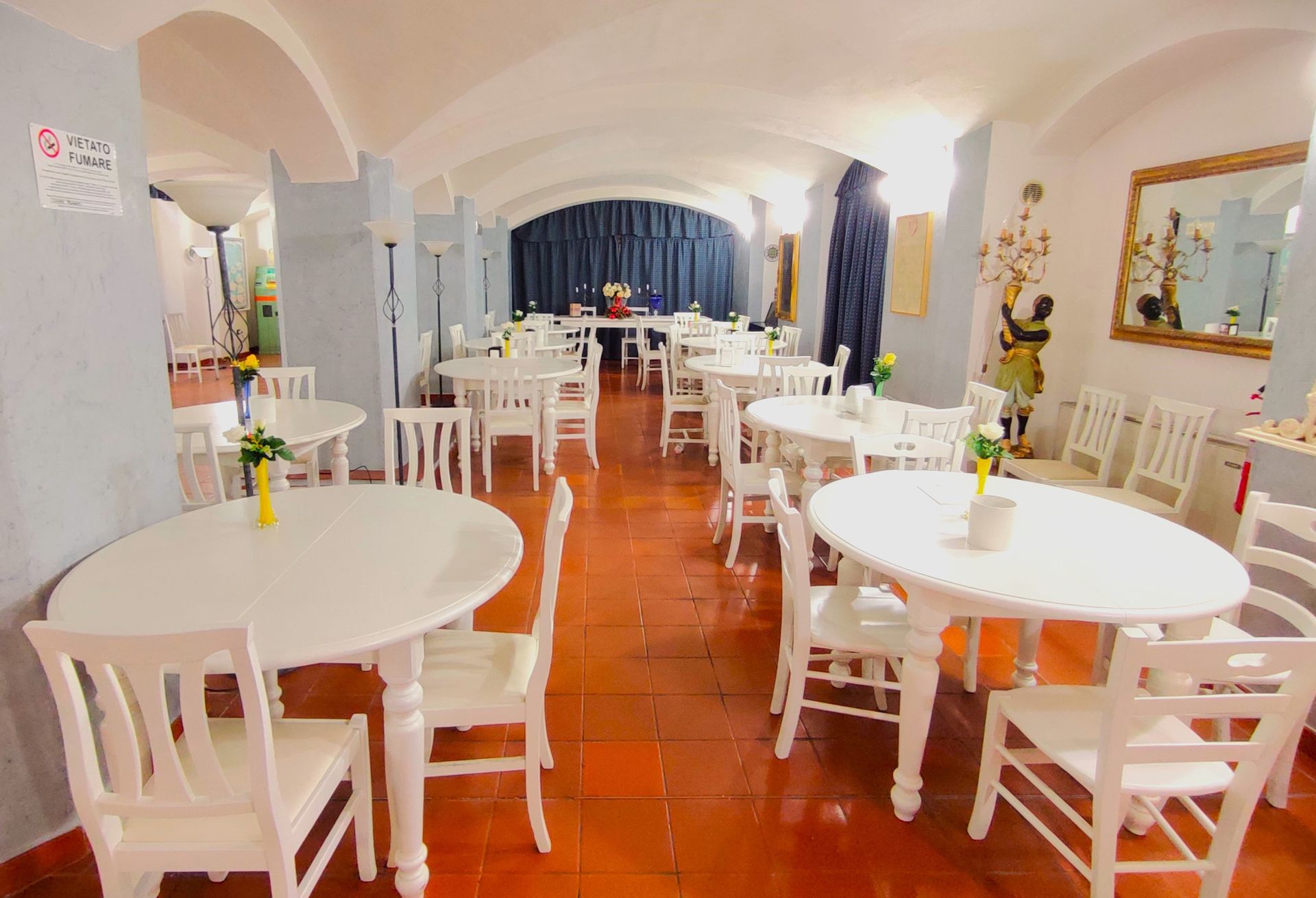 Bright white cafe with round tables and chairs on a glossy terracotta floor, viewed toward a curtained back wall