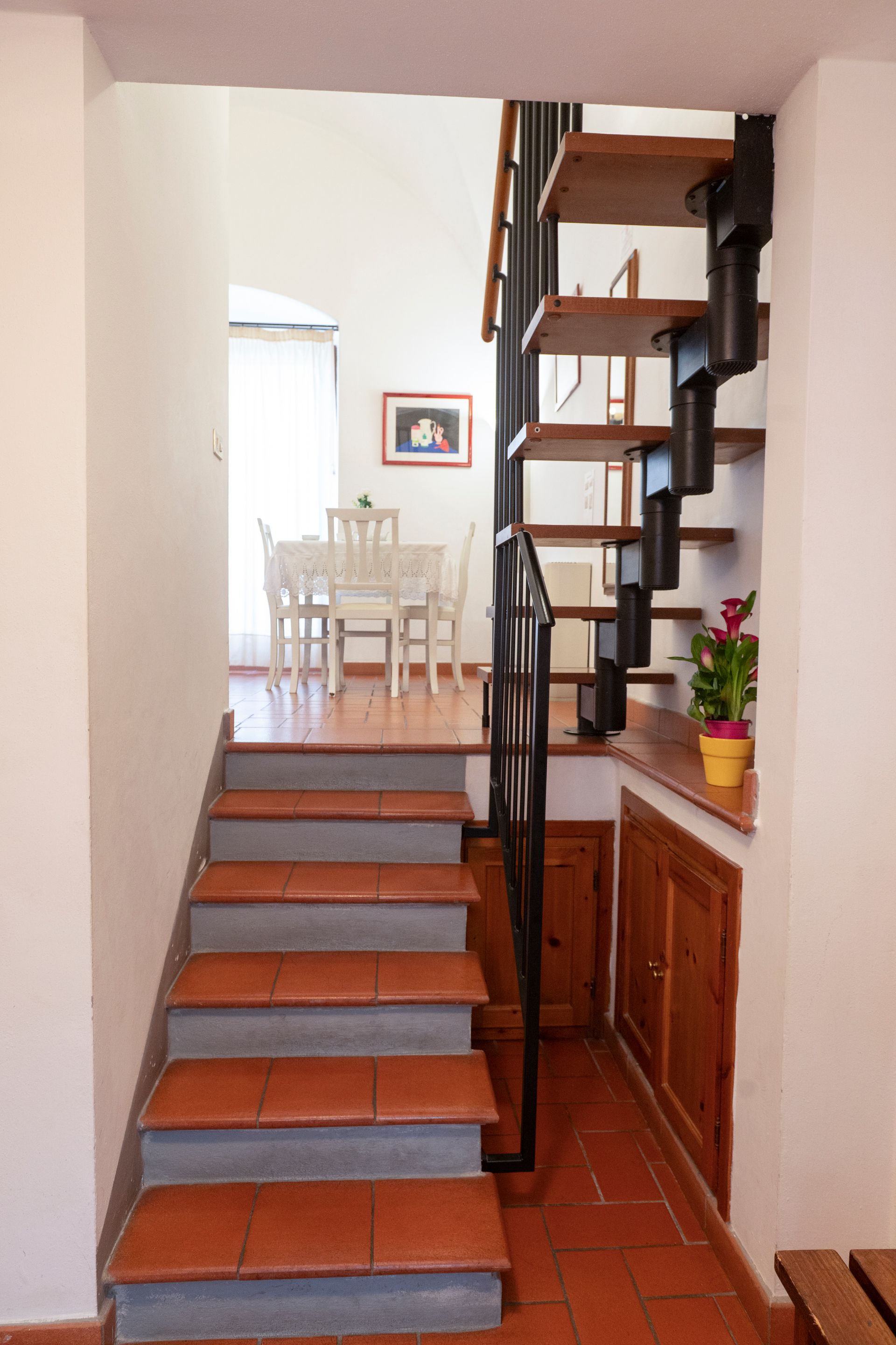 Narrow indoor stairway with terracotta tile steps, wooden railing, and dining area at the top.