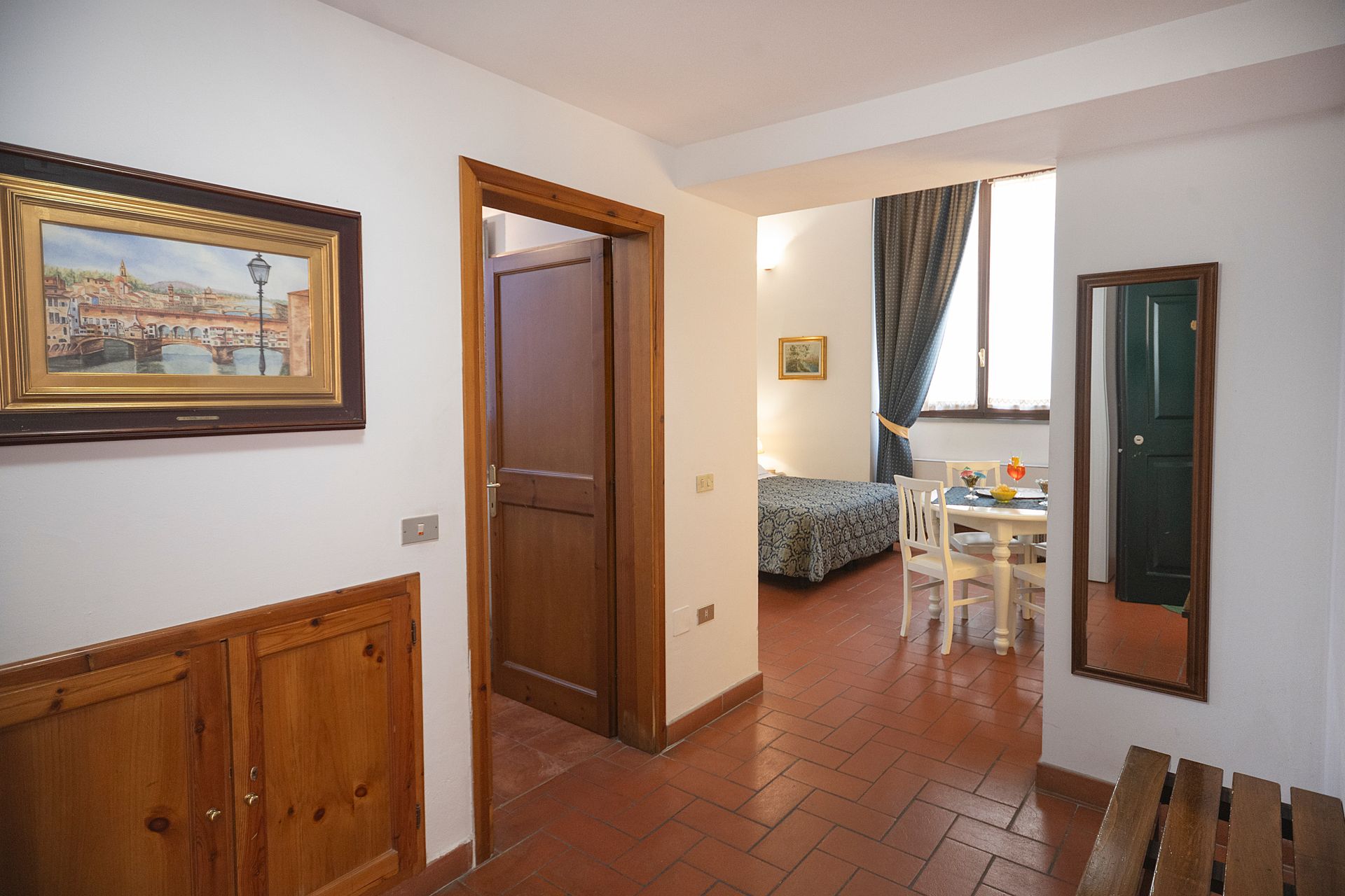 Small apartment hallway leading to a bedroom and dining nook, with terracotta tile and wooden doors.