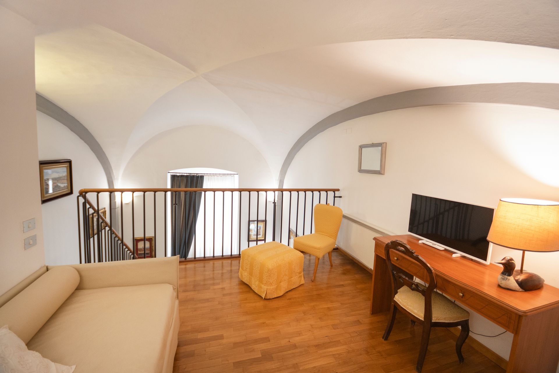 Bright loft room with desk, chair, lamp, ottoman, and sofa under arched white ceilings