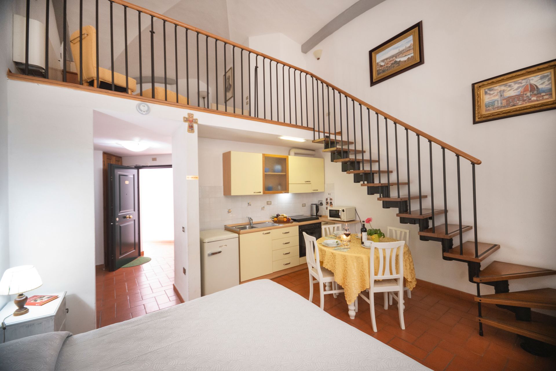 Bright loft kitchen and dining area with a staircase, white walls, and wooden railing.