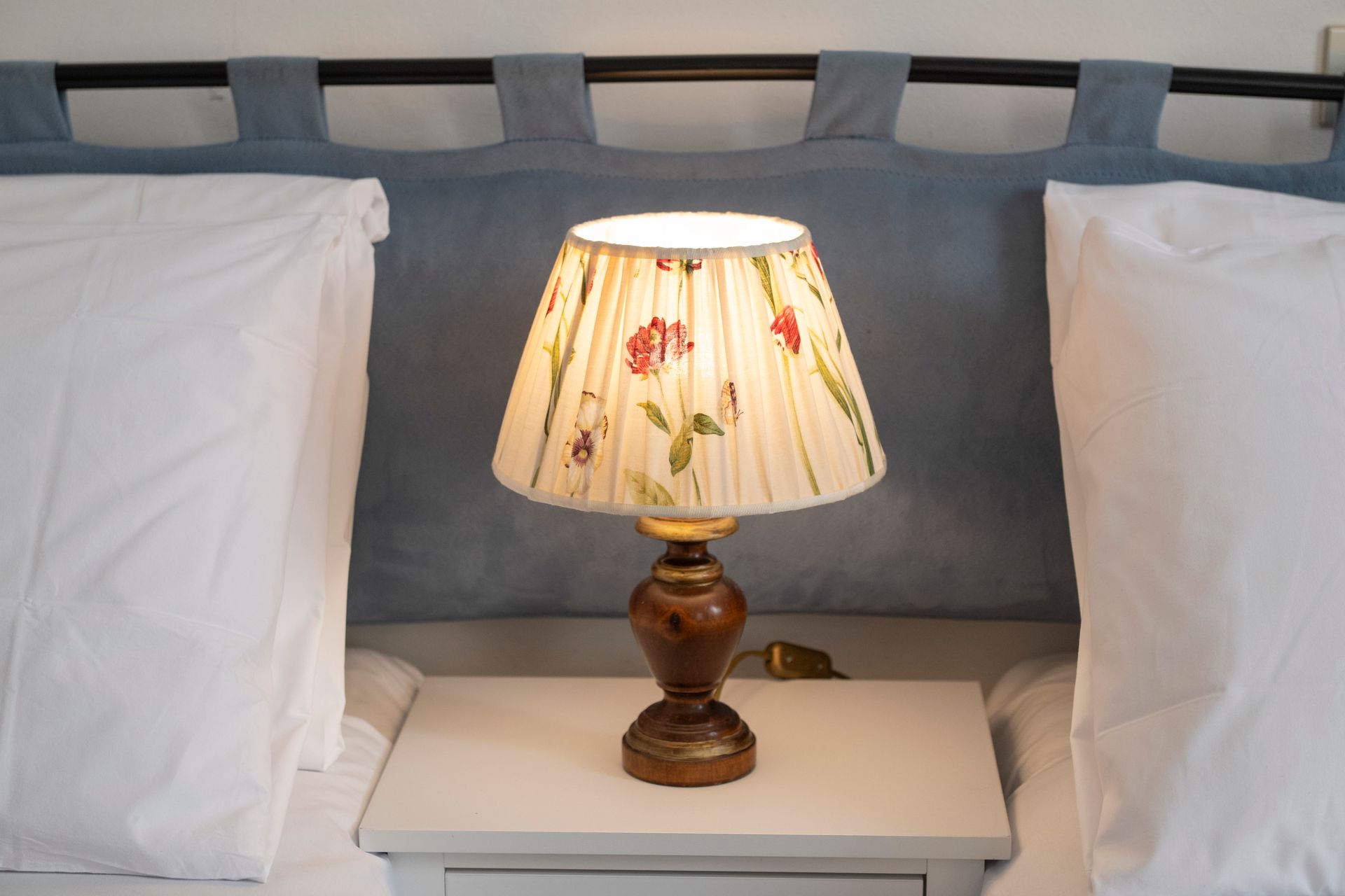 Bedside lamp with floral shade between two white pillows on a bed