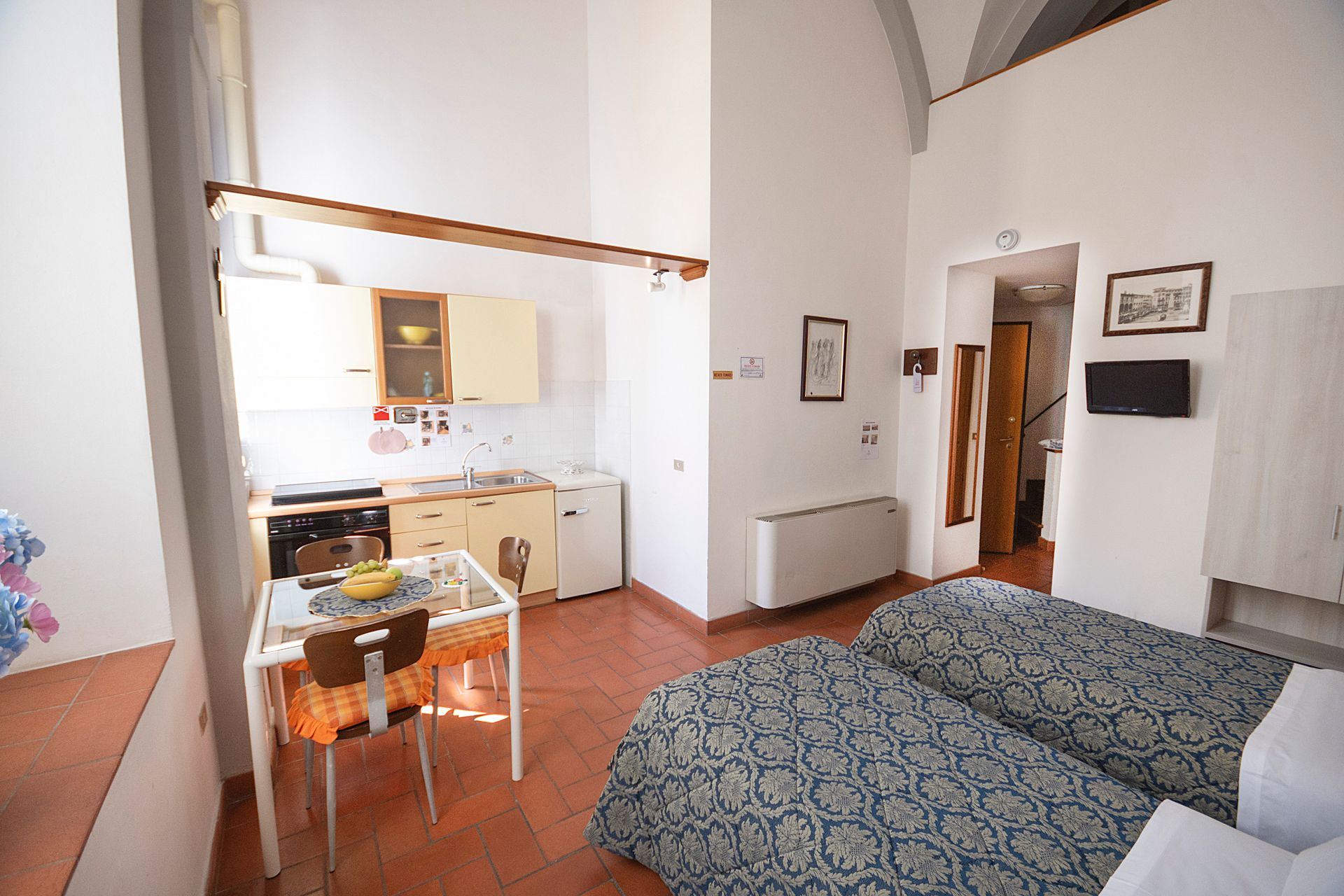 Small studio apartment with bed, dining table, kitchenette, and arched white walls