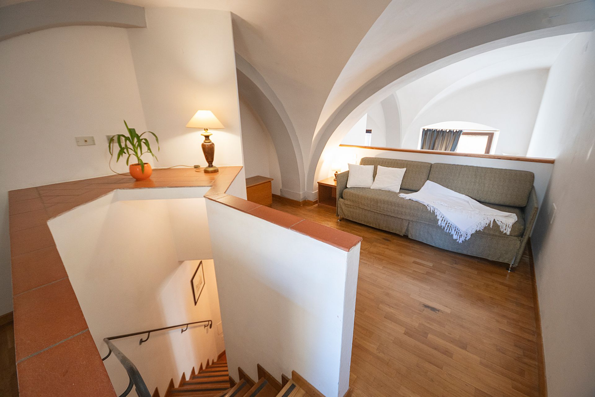 Attic staircase and bedroom with white vaulted ceilings, wood floor, and a bed by the wall