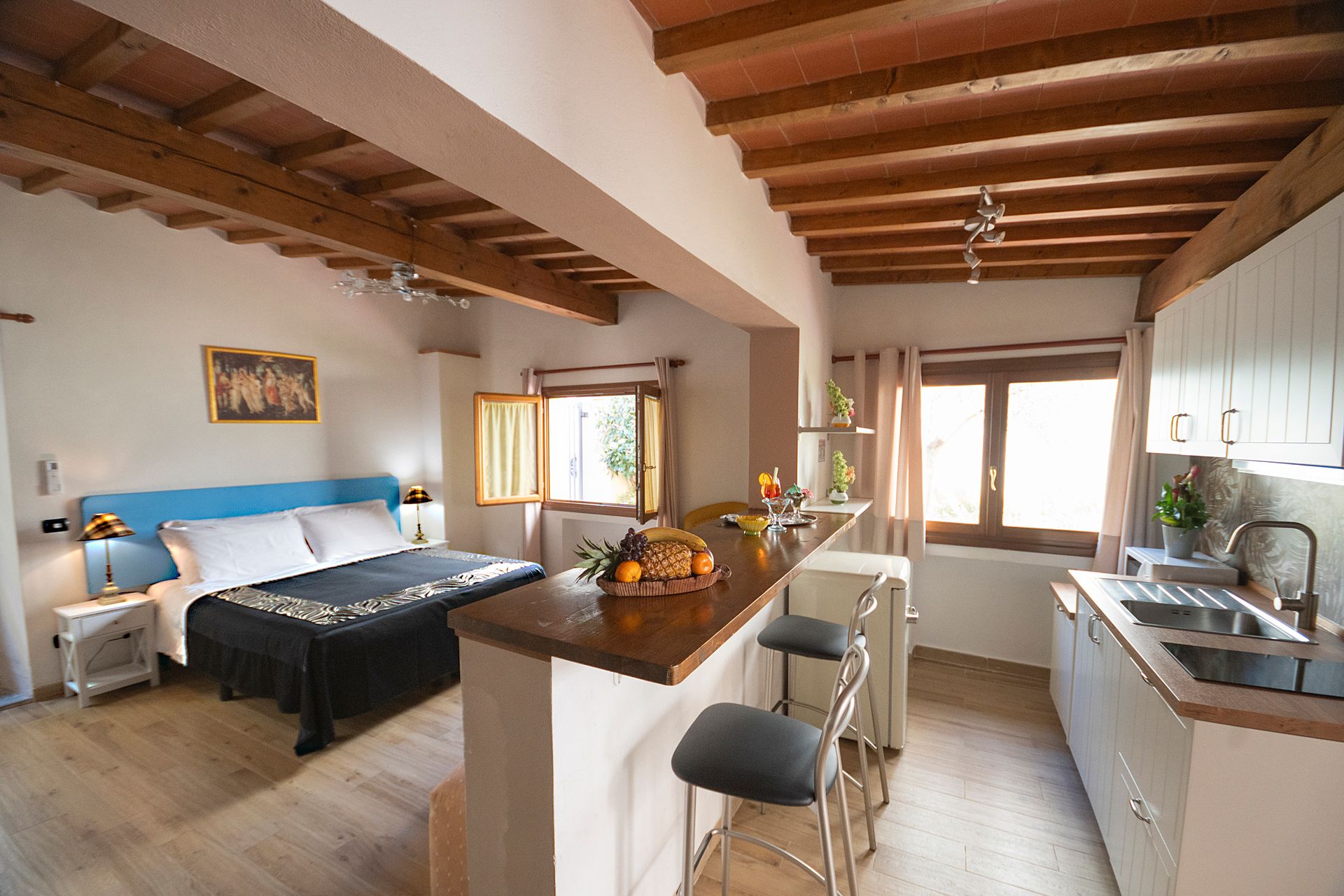 Cozy studio apartment with bed, kitchen, dining table, exposed wood beams, and large windows