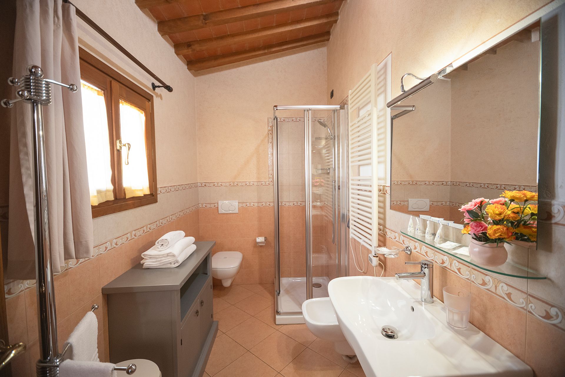 Modern bathroom with sink, shower, window, and towel rack, in warm beige tones.