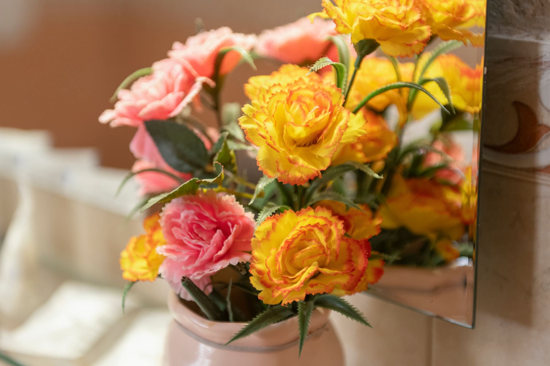 Bouquet of pink and yellow flowers in a vase on a shelf near a mirror